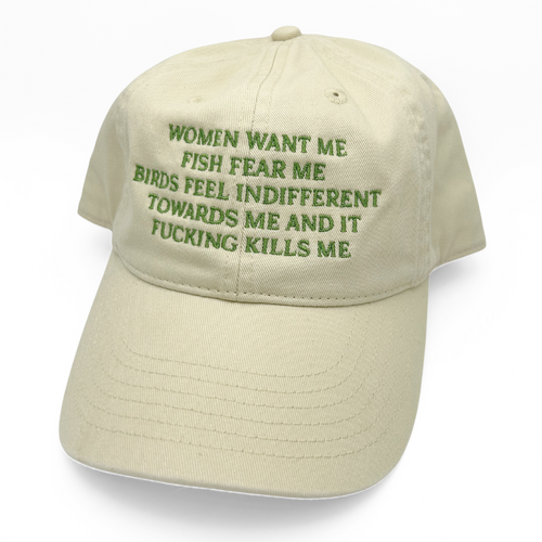 A light beige baseball cap with green embroidered text on the front that reads, 'WOMEN WANT ME FISH FEAR ME BIRDS FEEL INDIFFERENT TOWARDS ME AND IT FUCKING KILLS ME.'.